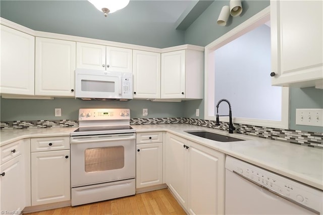 kitchen with a sink, white appliances, light countertops, and white cabinetry