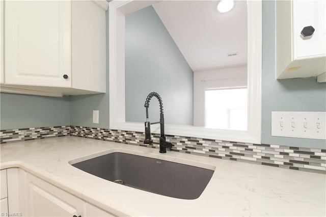 kitchen featuring tasteful backsplash, white cabinetry, light stone counters, and a sink