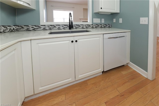 kitchen featuring a sink, backsplash, light wood-style floors, white cabinets, and white dishwasher