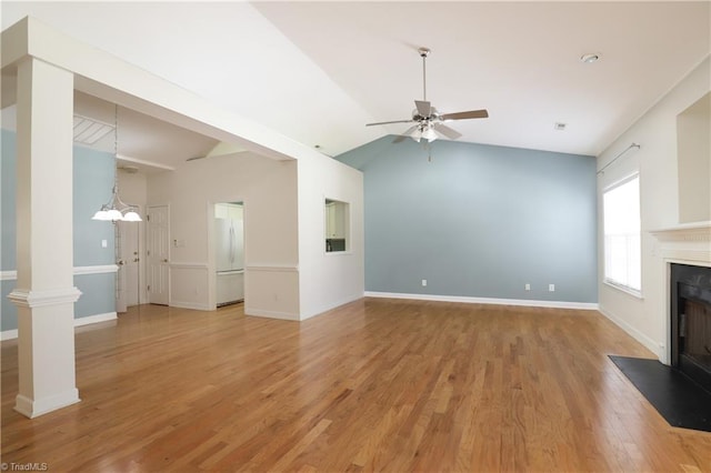 unfurnished living room with ornate columns, a fireplace with flush hearth, vaulted ceiling, ceiling fan with notable chandelier, and light wood-type flooring