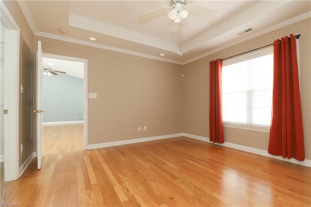 empty room with a tray ceiling, light wood-style floors, visible vents, and ceiling fan