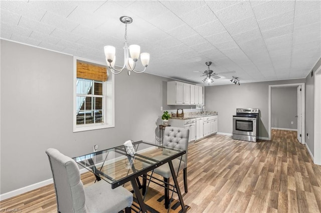 dining space featuring sink, wood-type flooring, and ceiling fan with notable chandelier