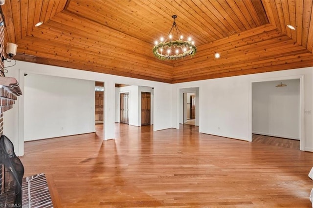 unfurnished living room featuring a towering ceiling, wood ceiling, light hardwood / wood-style floors, a chandelier, and a brick fireplace