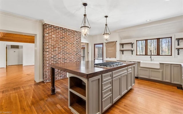 kitchen featuring wood counters, a kitchen island, sink, stainless steel gas stovetop, and gray cabinetry