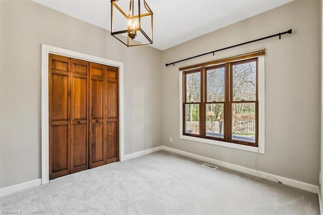 unfurnished bedroom with light carpet, an inviting chandelier, and a closet