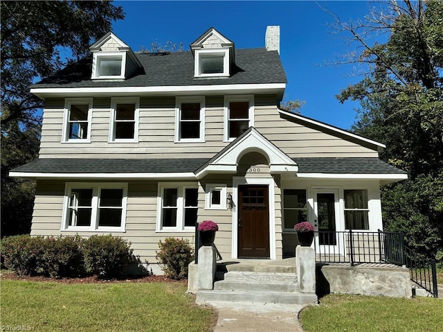 view of front of property with a shingled roof, a chimney, and a front lawn