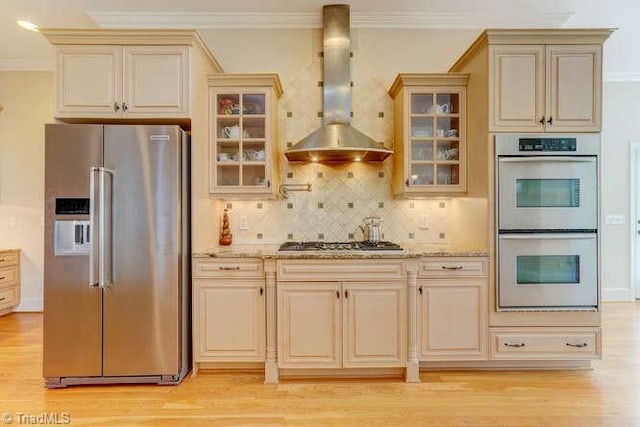 kitchen with cream cabinetry, appliances with stainless steel finishes, crown molding, and wall chimney range hood