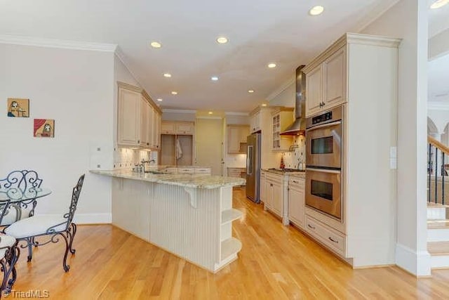 kitchen with a breakfast bar, ornamental molding, stainless steel appliances, light wood-style floors, and a peninsula