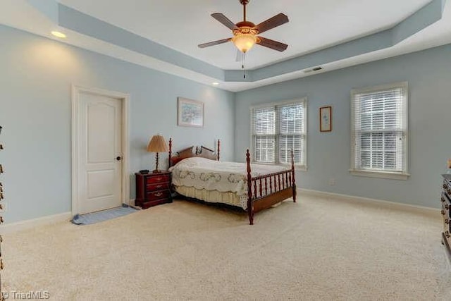 bedroom featuring a tray ceiling, visible vents, baseboards, and light carpet