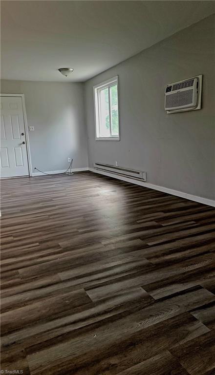 2410 Madre Pl, Greensboro, NC 27406 - spare room with a baseboard radiator, dark wood-style flooring, an AC wall unit, and baseboards