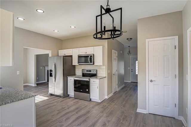 kitchen with decorative backsplash, light hardwood / wood-style floors, white cabinetry, stainless steel appliances, and a chandelier