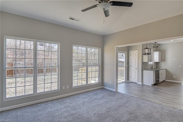 unfurnished living room with carpet flooring, sink, a healthy amount of sunlight, and ceiling fan with notable chandelier