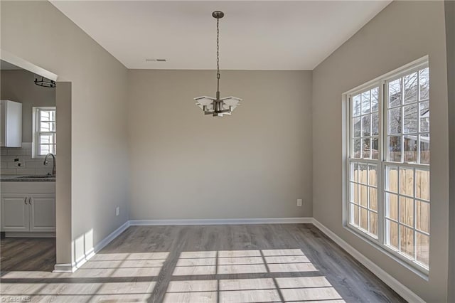 unfurnished dining area featuring sink, hardwood / wood-style floors, and an inviting chandelier