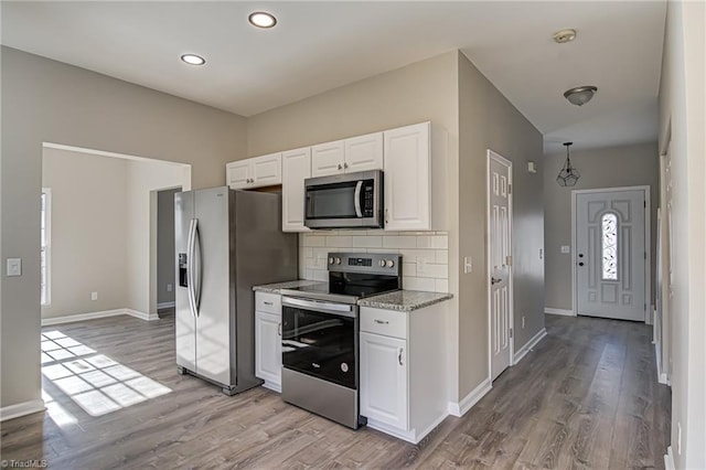 kitchen with backsplash, appliances with stainless steel finishes, light hardwood / wood-style floors, light stone counters, and white cabinetry