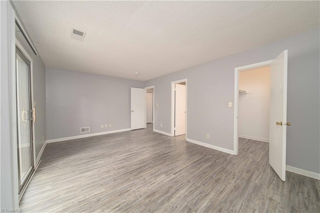 unfurnished bedroom with wood finished floors, baseboards, a spacious closet, a textured ceiling, and a closet