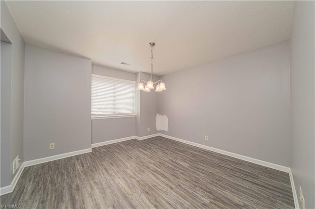 unfurnished room with wood finished floors, a chandelier, and baseboards