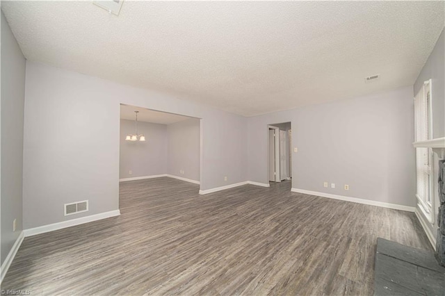 unfurnished living room featuring dark wood-style flooring, a textured ceiling, a chandelier, baseboards, and a fireplace