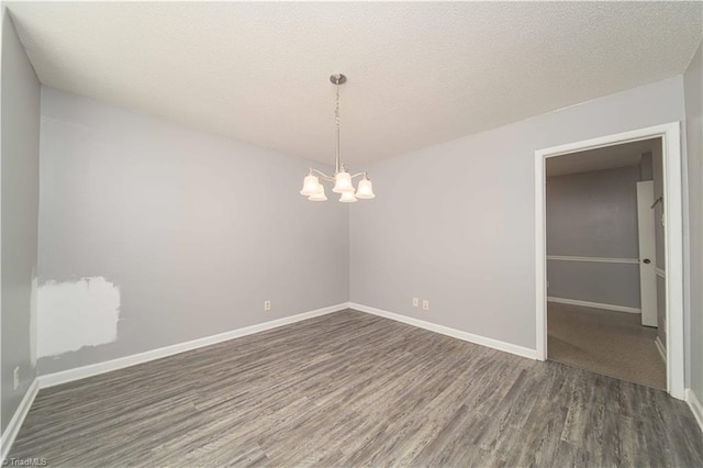 empty room with wood finished floors, a chandelier, baseboards, and a textured ceiling