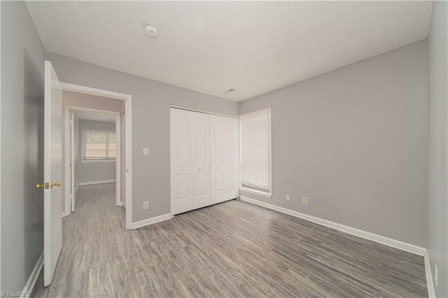 unfurnished bedroom with baseboards, wood finished floors, and a closet