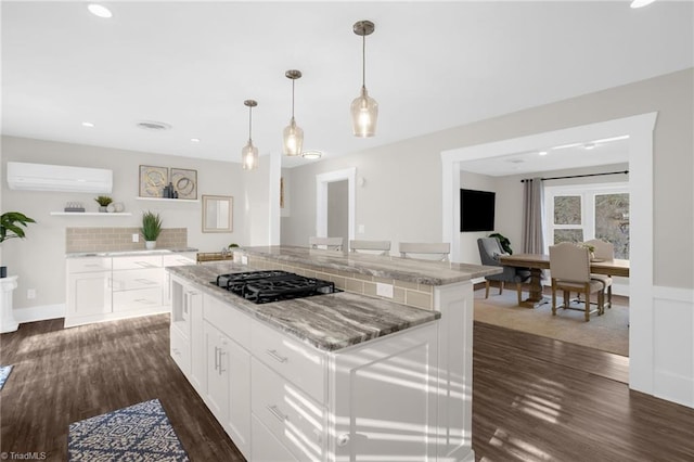 kitchen featuring an AC wall unit, a kitchen island, pendant lighting, white cabinetry, and black gas stovetop