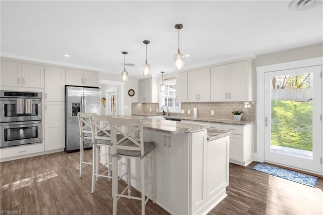 kitchen featuring white cabinetry, hanging light fixtures, stainless steel appliances, light stone countertops, and a kitchen island