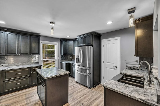 kitchen featuring sink, stainless steel fridge, light stone countertops, and light wood-type flooring