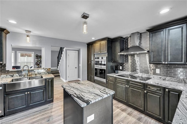 kitchen featuring sink, appliances with stainless steel finishes, a center island, light stone countertops, and wall chimney exhaust hood