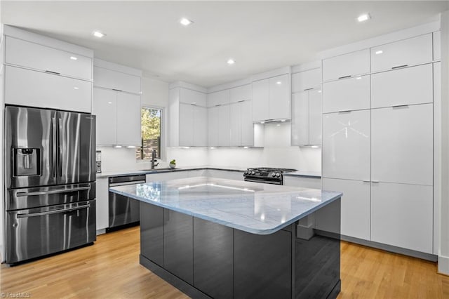 kitchen with white cabinets, stainless steel appliances, sink, light hardwood / wood-style floors, and a center island