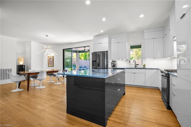 kitchen featuring a healthy amount of sunlight, white cabinetry, black gas range, pendant lighting, and stainless steel fridge with ice dispenser