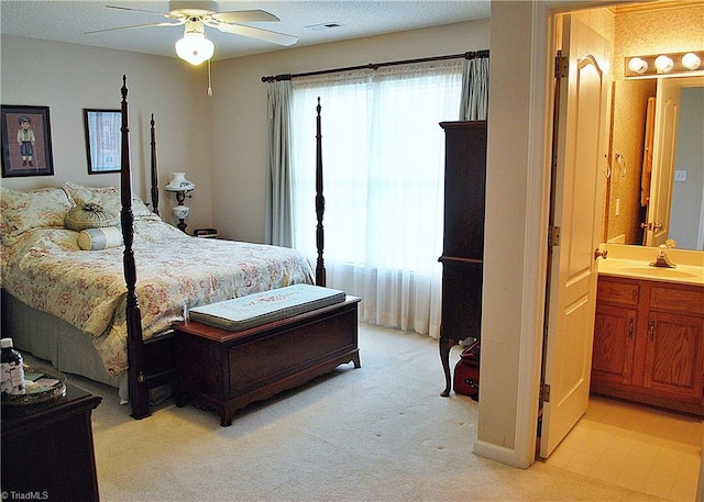 bedroom with a ceiling fan, a sink, ensuite bathroom, visible vents, and light carpet