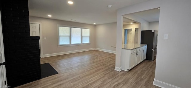 kitchen with stainless steel refrigerator, light wood-type flooring, light stone counters, and white cabinets