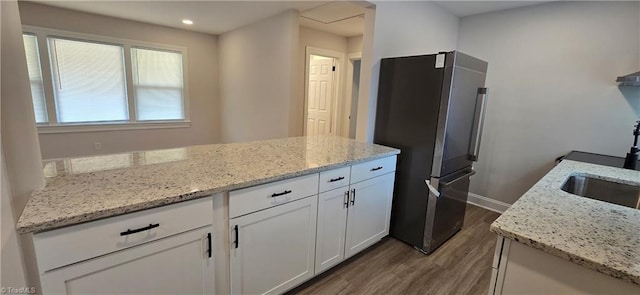 kitchen featuring white cabinets, light stone countertops, hardwood / wood-style flooring, and stainless steel fridge