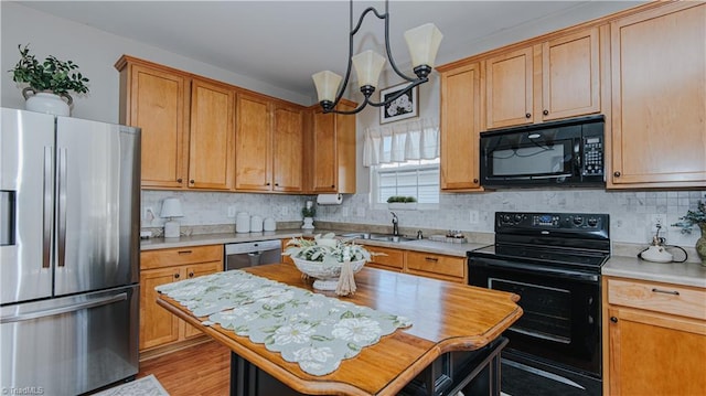 kitchen featuring light countertops, decorative backsplash, an inviting chandelier, black appliances, and a sink