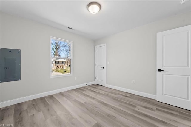 empty room featuring electric panel, visible vents, baseboards, and light wood-type flooring