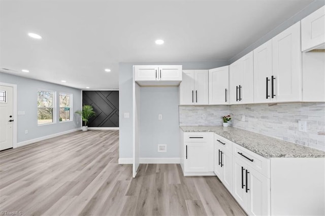 kitchen featuring white cabinetry, light stone countertops, light wood-style floors, and tasteful backsplash