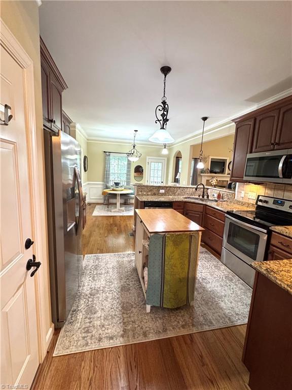 kitchen featuring dark wood-type flooring, stainless steel appliances, sink, hanging light fixtures, and a kitchen island with sink