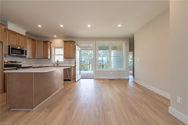 kitchen featuring light wood finished floors, a center island, stainless steel appliances, brown cabinetry, and light countertops