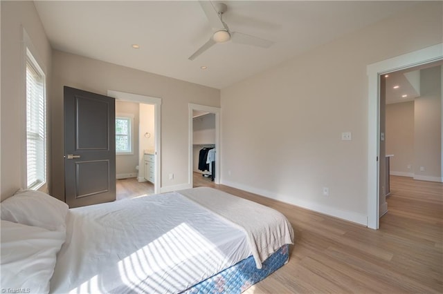 bedroom featuring a walk in closet, ensuite bathroom, recessed lighting, light wood-style floors, and baseboards