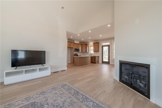 unfurnished living room with baseboards, light wood-type flooring, recessed lighting, a glass covered fireplace, and high vaulted ceiling