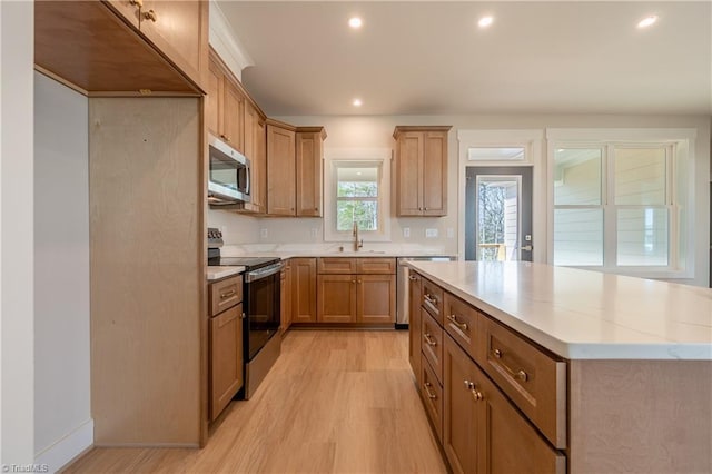 kitchen featuring light wood finished floors, a kitchen island, recessed lighting, a sink, and appliances with stainless steel finishes