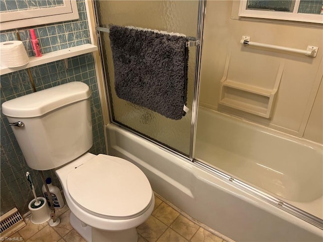 bathroom with enclosed tub / shower combo, toilet, and tile walls