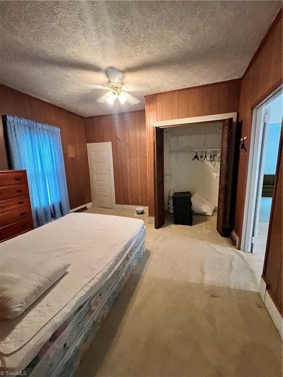 bedroom with wood walls, a closet, a ceiling fan, light colored carpet, and a textured ceiling