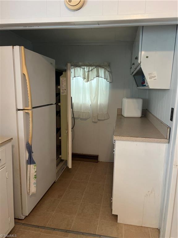 kitchen with freestanding refrigerator, light countertops, white cabinetry, and light tile patterned floors
