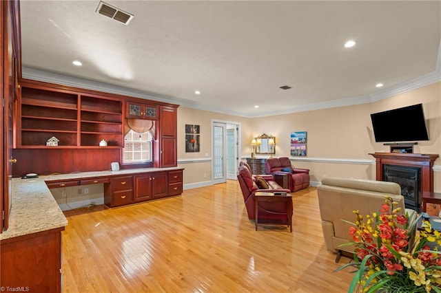 living room with light wood-style floors, ornamental molding, built in desk, and visible vents