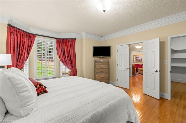 bedroom with crown molding, baseboards, light wood-type flooring, and a textured ceiling