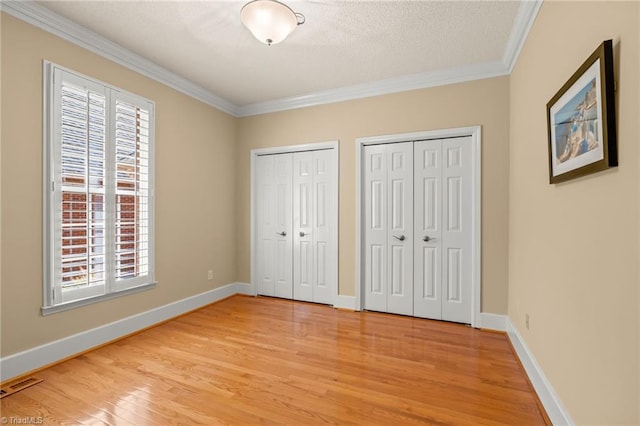 unfurnished bedroom with two closets, visible vents, ornamental molding, and light wood-style flooring
