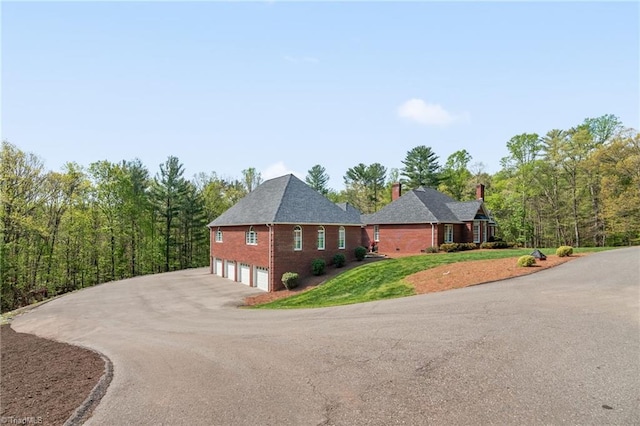 view of side of home featuring a lawn, a chimney, brick siding, an attached garage, and driveway