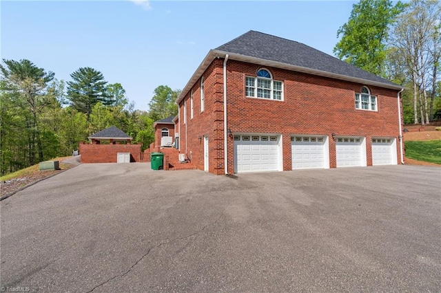 view of side of home featuring brick siding, an attached garage, and aphalt driveway