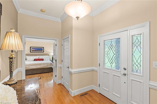 entryway with crown molding, baseboards, visible vents, and light wood-style flooring