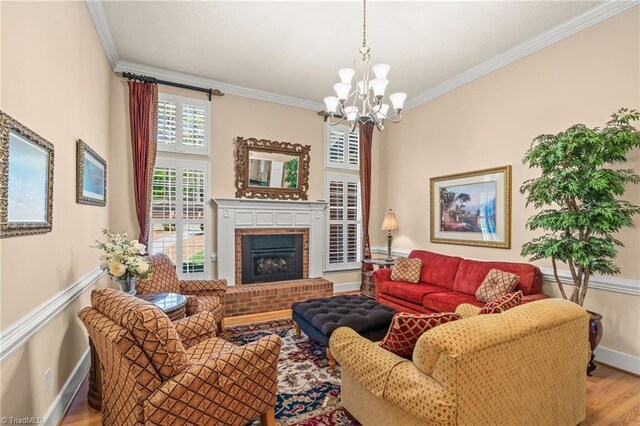 living room with crown molding, a brick fireplace, wood finished floors, baseboards, and a chandelier